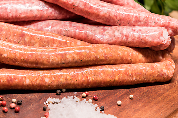 Image showing raw sausages with chilli and herbs on a wooden board with spices