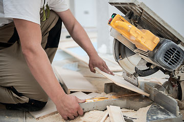 Image showing Man cutting laminate floor plank with electrical circular saw