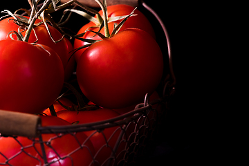 Image showing big red tomatoes on black background in light dark ready to cook
