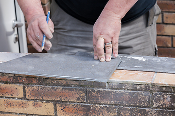 Image showing the tiler measures and puts marks to cut and lay a tile