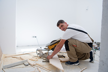 Image showing Man cutting laminate floor plank with electrical circular saw