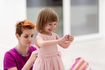 Image showing young mother helping daughter while putting on a dress