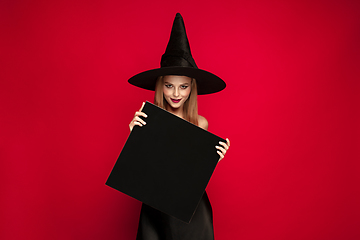 Image showing Young woman in hat as a witch on red background