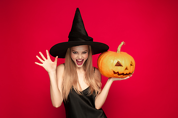 Image showing Young woman in hat as a witch on red background