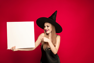 Image showing Young woman in hat as a witch on red background