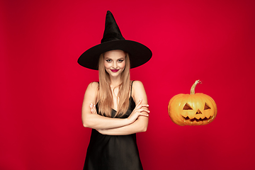 Image showing Young woman in hat as a witch on red background