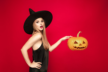 Image showing Young woman in hat as a witch on red background