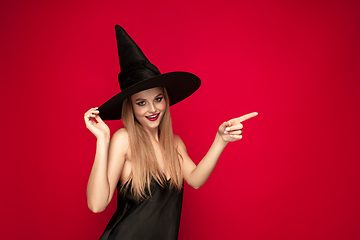 Image showing Young woman in hat as a witch on red background