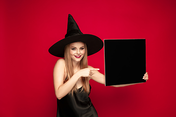 Image showing Young woman in hat as a witch on red background