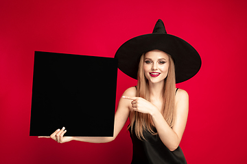 Image showing Young woman in hat as a witch on red background