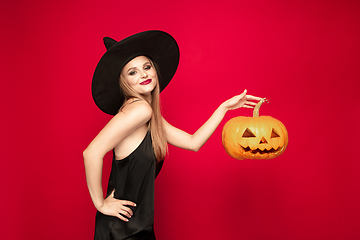 Image showing Young woman in hat as a witch on red background