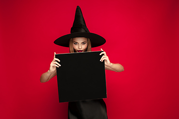 Image showing Young woman in hat as a witch on red background