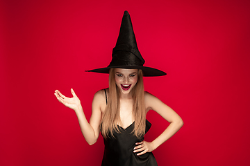 Image showing Young woman in hat as a witch on red background