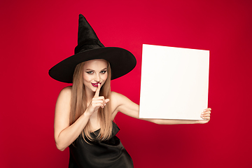 Image showing Young woman in hat as a witch on red background