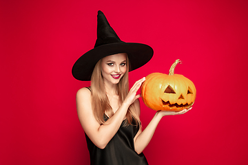 Image showing Young woman in hat as a witch on red background