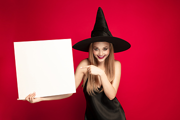 Image showing Young woman in hat as a witch on red background