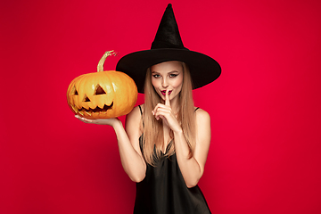 Image showing Young woman in hat as a witch on red background