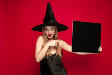 Image showing Young woman in hat as a witch on red background