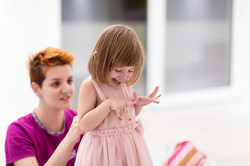 Image showing young mother helping daughter while putting on a dress