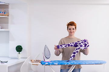 Image showing Red haired woman ironing clothes at home