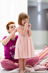 Image showing young mother helping daughter while putting on a dress