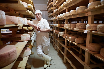 Image showing Cheese maker at the storage with shelves full of cow and goat cheese