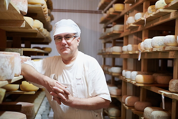 Image showing Cheese maker at the storage with shelves full of cow and goat cheese