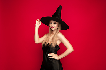 Image showing Young woman in hat as a witch on red background