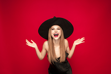 Image showing Young woman in hat as a witch on red background