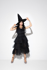 Image showing Young woman in hat and dress as a witch on white background