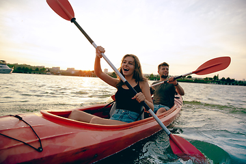 Image showing Confident young couple kayaking on river together with sunset on the background