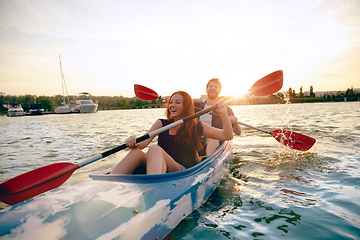 Image showing Confident young couple kayaking on river together with sunset on the background