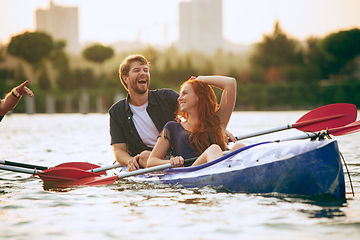 Image showing Confident young couple kayaking on river together with sunset on the background