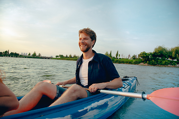 Image showing Confident young man kayaking on river with sunset on the background