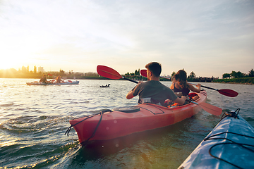 Image showing Confident young couple kayaking on river together with sunset on the background