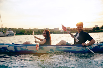 Image showing Confident young couple kayaking on river together with sunset on the background