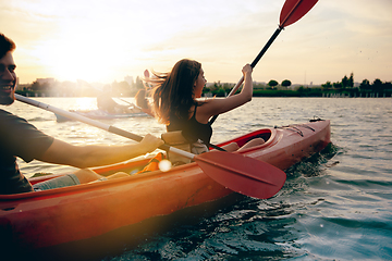 Image showing Confident young couple kayaking on river together with sunset on the background