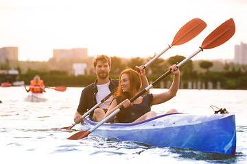 Image showing Confident young couple kayaking on river together with sunset on the background