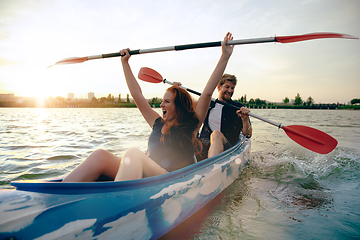 Image showing Confident young couple kayaking on river together with sunset on the background