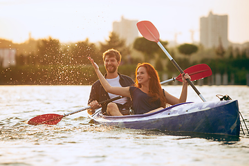 Image showing Confident young couple kayaking on river together with sunset on the background