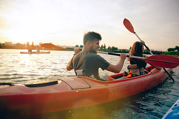 Image showing Confident young couple kayaking on river together with sunset on the background