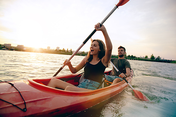 Image showing Confident young couple kayaking on river together with sunset on the background