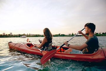 Image showing Confident young couple kayaking on river together with sunset on the background