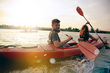 Image showing Confident young couple kayaking on river together with sunset on the background