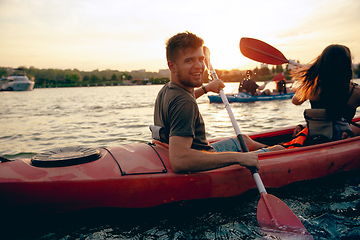 Image showing Confident young couple kayaking on river together with sunset on the background