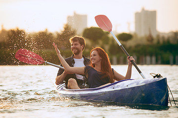 Image showing Confident young couple kayaking on river together with sunset on the background