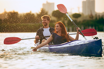 Image showing Confident young couple kayaking on river together with sunset on the background