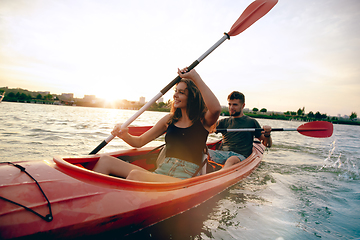 Image showing Confident young couple kayaking on river together with sunset on the background