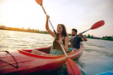 Image showing Confident young couple kayaking on river together with sunset on the background