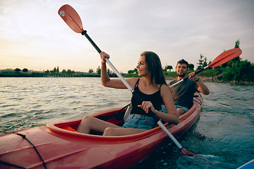 Image showing Confident young couple kayaking on river together with sunset on the background